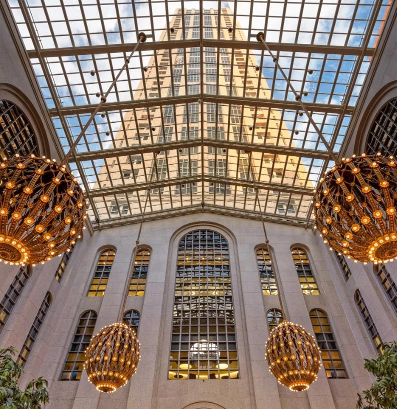 The skylit atrium of the firm’s Atlanta office building — a glazed roof framing the tower above, with brass chandeliers suspended over limestone arches